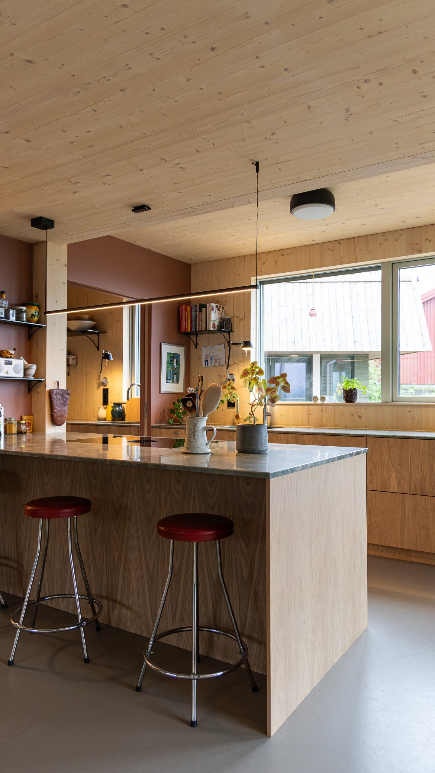 Köksö med häll, stenskiva och barstolar framför ett stort fönster och en lång bänkrad. Köksö med häll, stenskiva och barstolar framför ett stort fönster och en lång bänkrad.